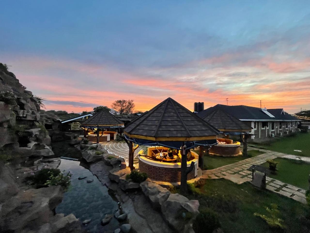 Gazebos, amphitheatre steps and landscaped rock stream under a pink and orange sky