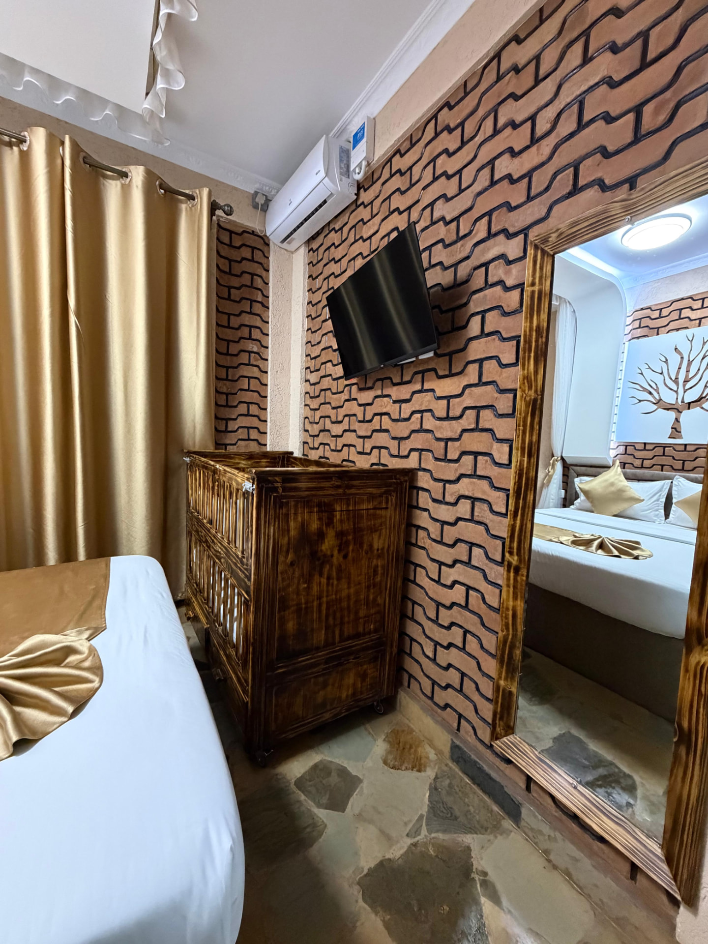 Guest room bed with gold linens and carved wooden cabinet at Mawimbi Jiko