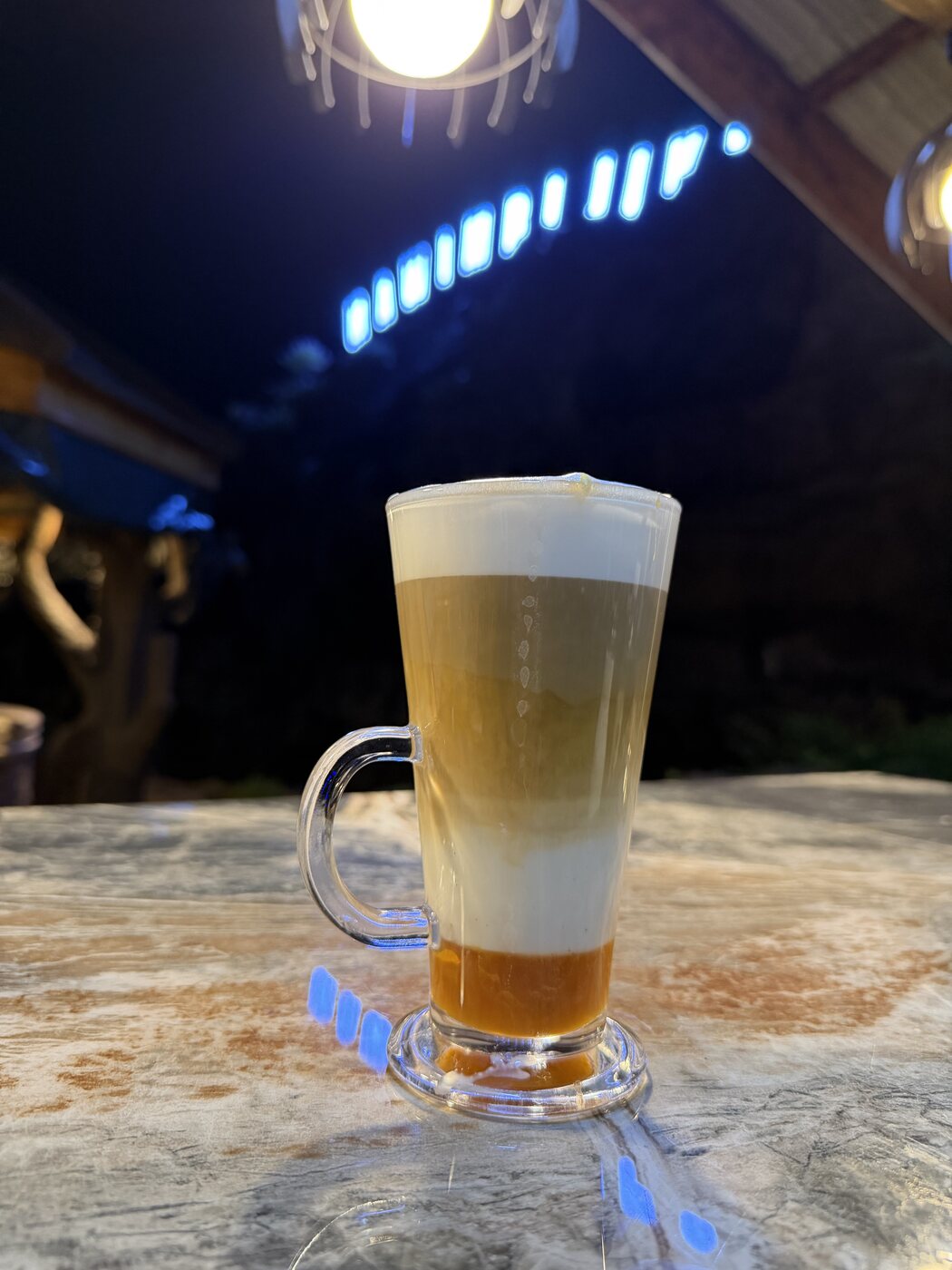 Layered caramel macchiato in a tall glass on a marble table under warm evening lights