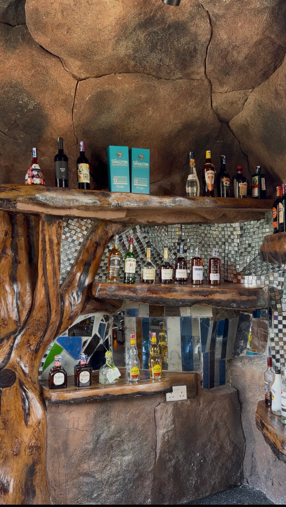 Spirits and wine bottles displayed against the rugged rock wall and shimmering mosaic tiles