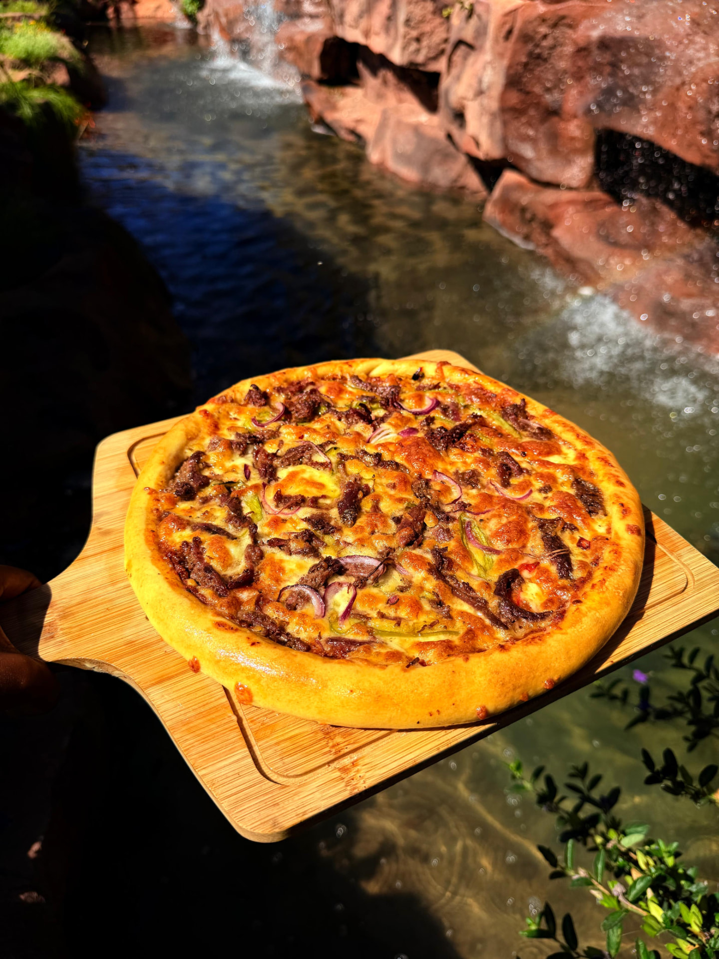 Freshly baked pizza held beside the Mawimbi Jiko waterfall feature