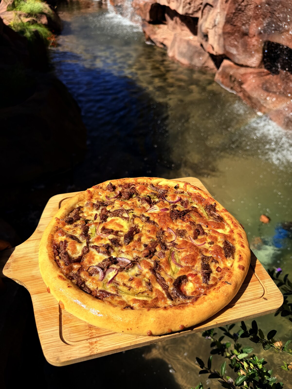 Oven-baked pizza on a wooden board beside the Mawimbi Jiko rock waterfall