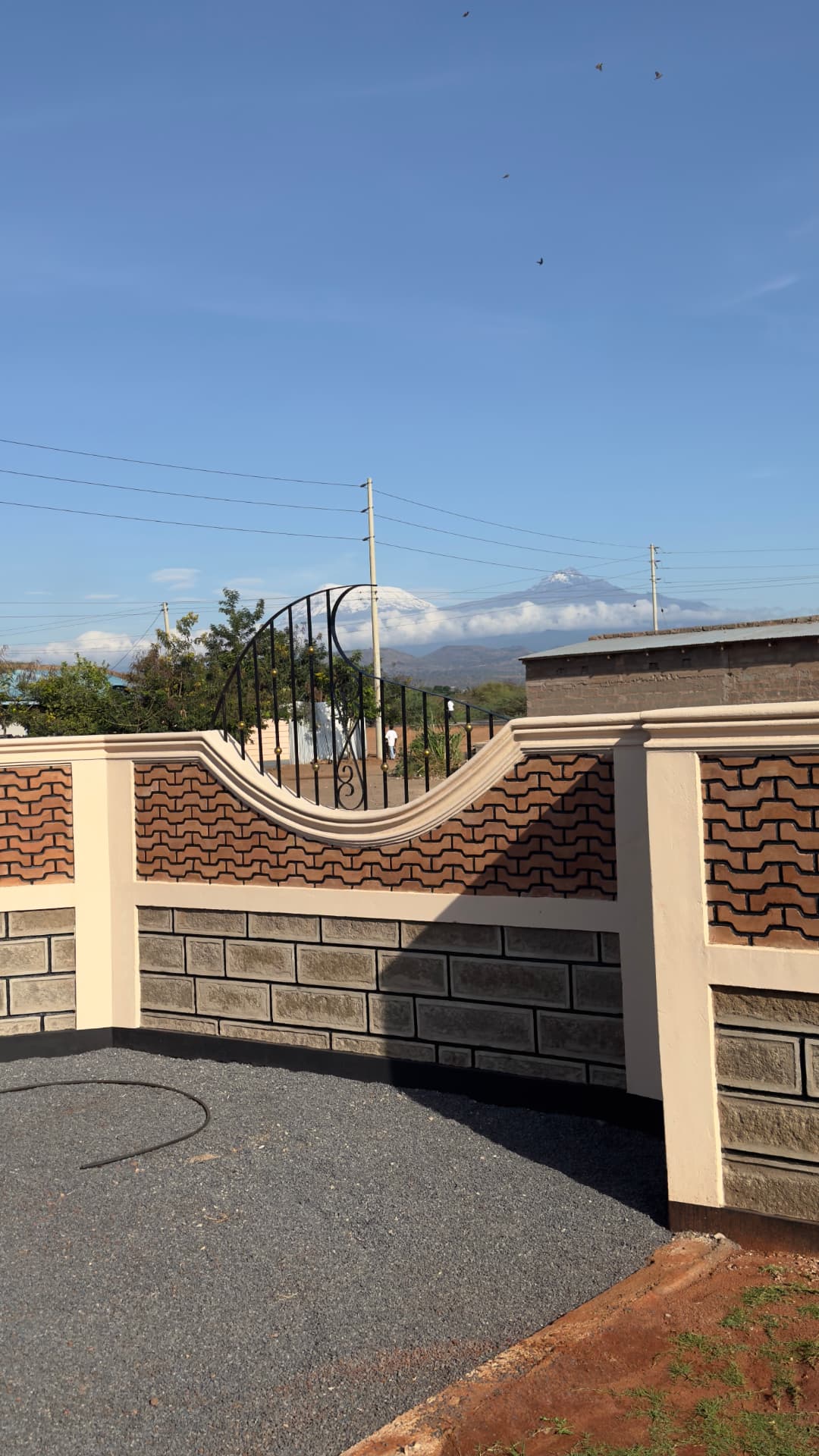 Snow-capped Mount Kilimanjaro seen above the signature wave-brick perimeter wall at Mawimbi Jiko in Taveta.