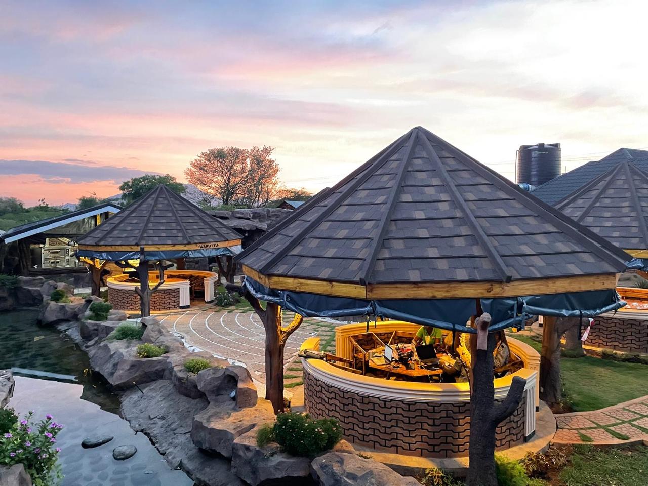 Warmly lit thatched-style gazebo dining pods beside the rock stream at sunset