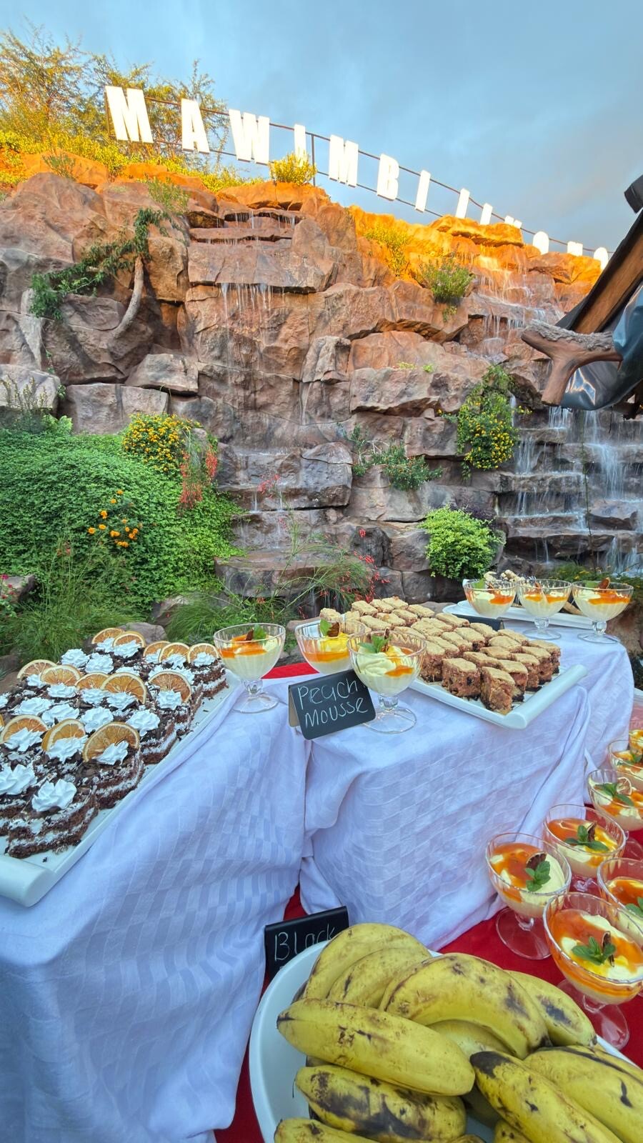 Buffet dessert and pastry display set beneath the illuminated Mawimbi Jiko waterfall sign