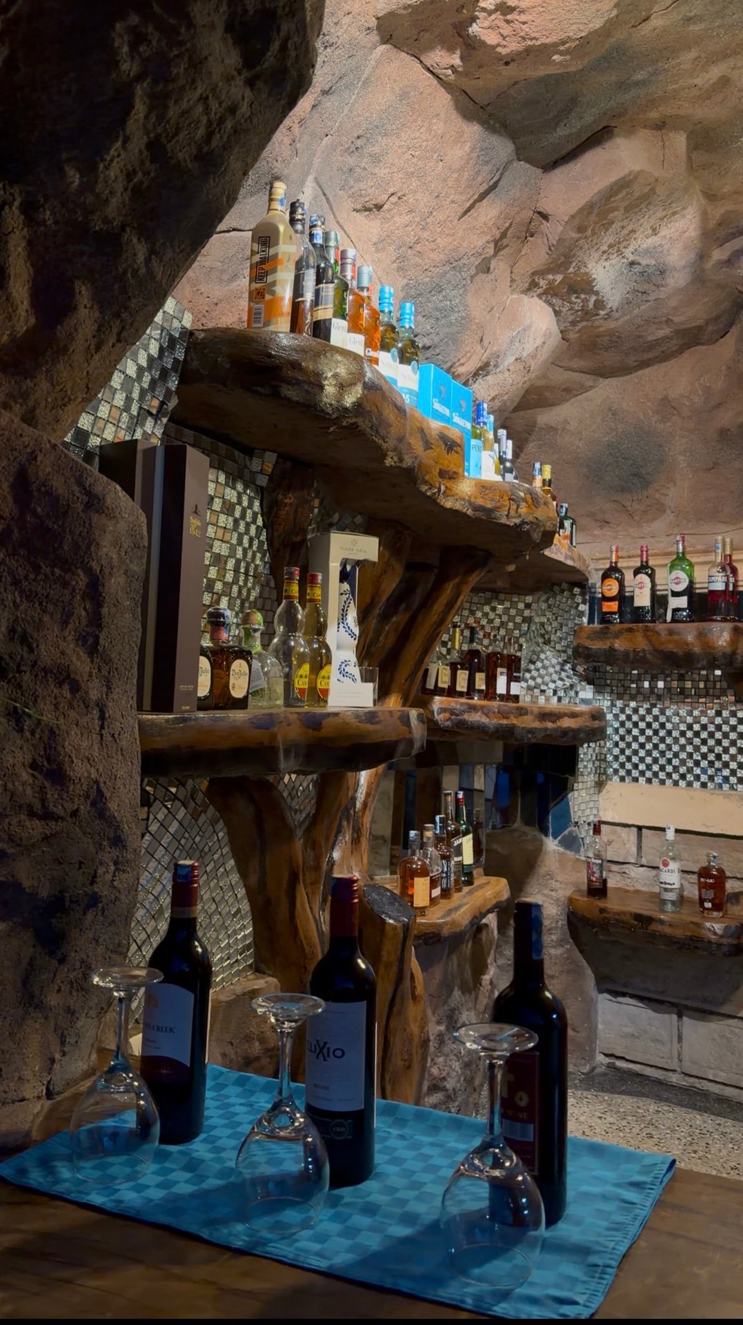 Backbar built into a cave-like rock alcove holding wines and spirits on thick timber shelves