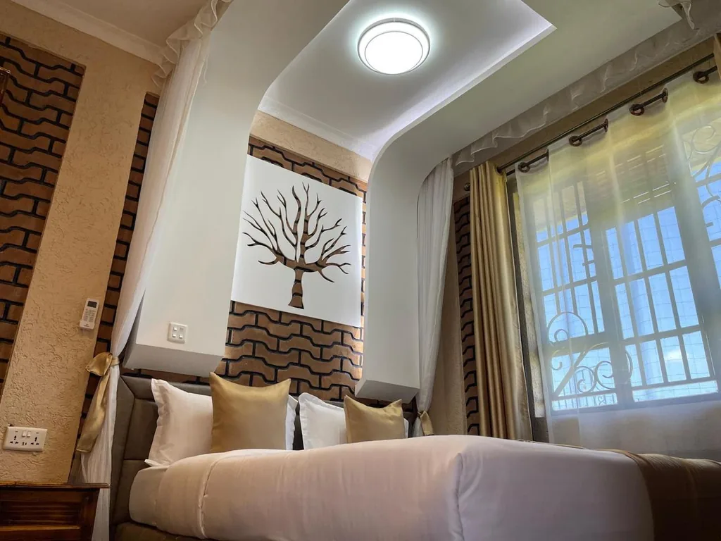 Bed dressed in white and gold beneath the recessed ceiling light and boabab wall art