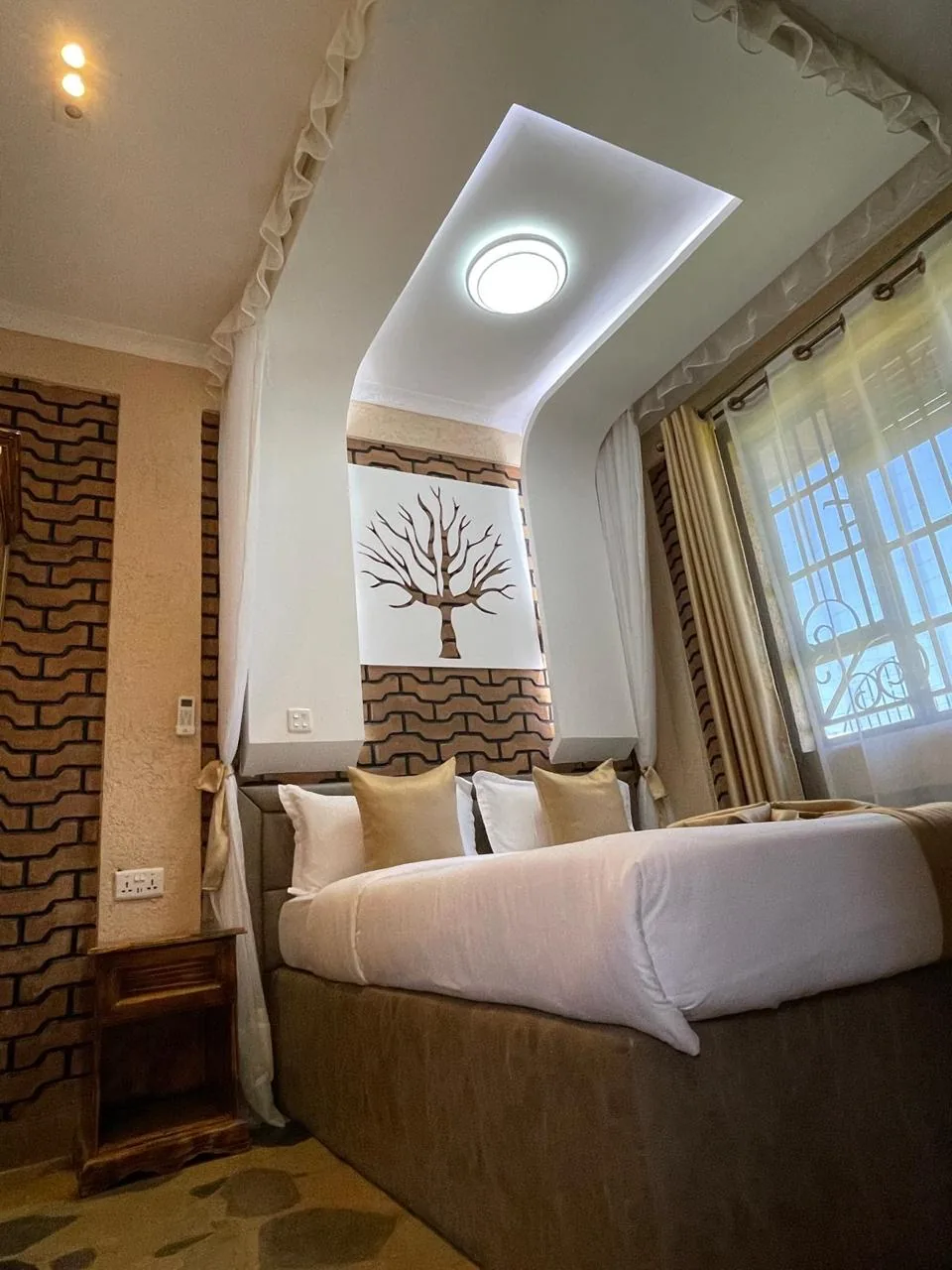 Corner view of a guest room with bedside cabinet, air-conditioning control and sheer canopy drapes