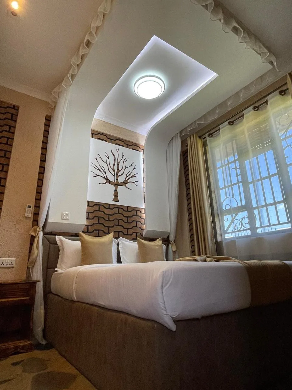 Guest room bed framed by curtains, with the signature boabab panel set into the brick wall