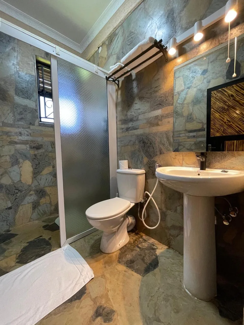 En-suite bathroom in natural stone with a walk-in shower, WC, pedestal basin and mirror